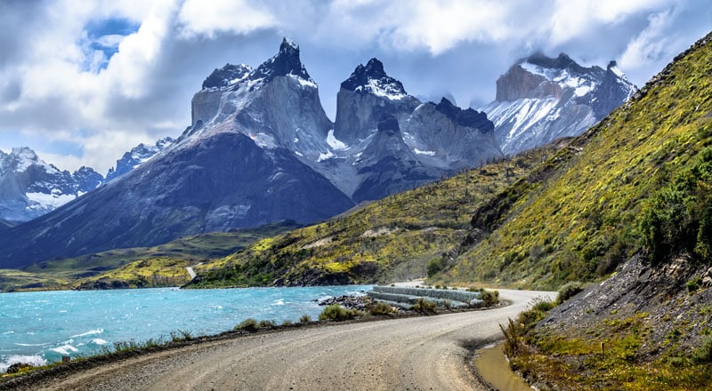 Carretera sinuosa a un costado de un lago con las torres del paine de fondo en la patagonia chilena